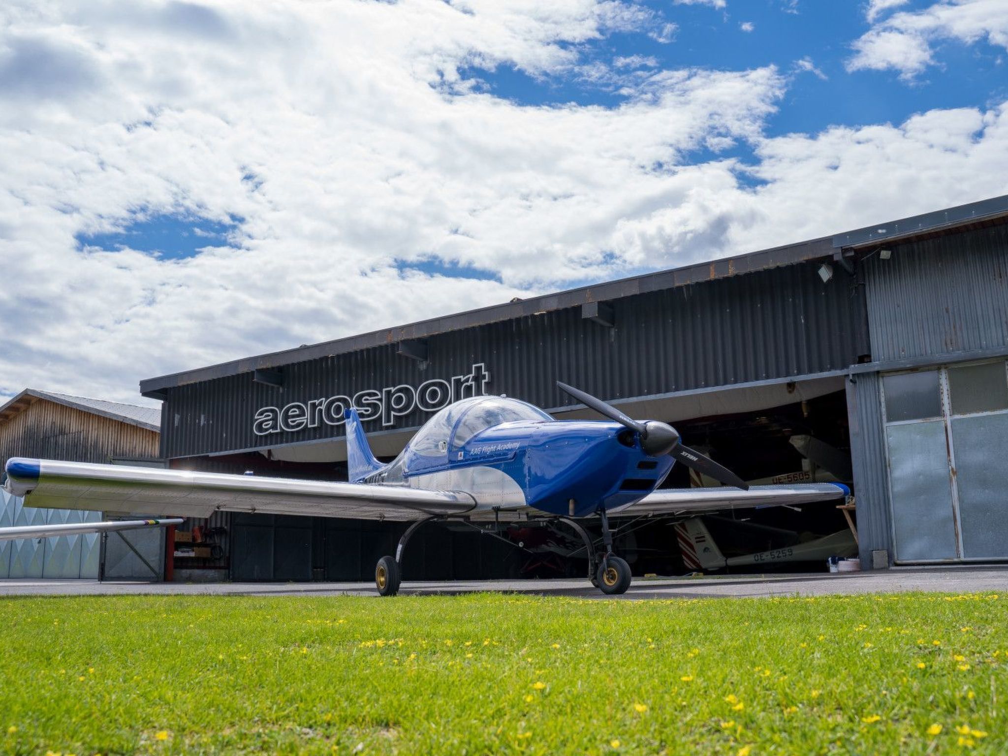 Ein kleines blaues Flugzeug vor einem Flughafenhangar.