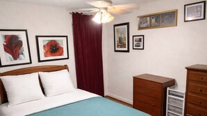 Un dormitorio con cama, ventilador de techo, cómoda y mesita de noche.