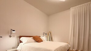 Un dormitorio con cama, lámparas de noche, mesita de noche, espejo e iluminación en el techo.