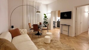 Una sala moderna con un sofá, otomanas, un comedor y un televisor.