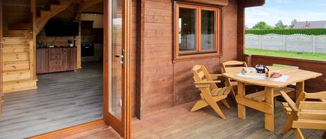 A wooden deck with a table and chairs, a sliding glass door leading to a kitchen, and a window with a view of the outside.