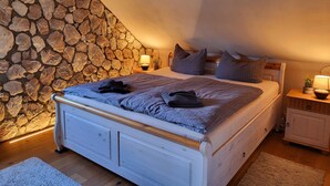 Un dormitorio con pared de piedra, una cama con almohadas, una mesita de noche con lámpara y un armario pequeño.