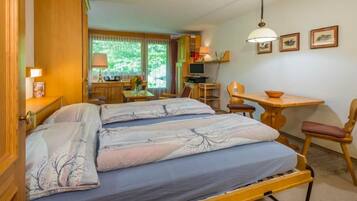 A cozy room with a bed, a desk, a chair, and a window with a view of greenery.