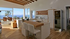 Une cuisine moderne dotée d’un îlot central, de tabourets de bar et offrant une vue sur l’océan.