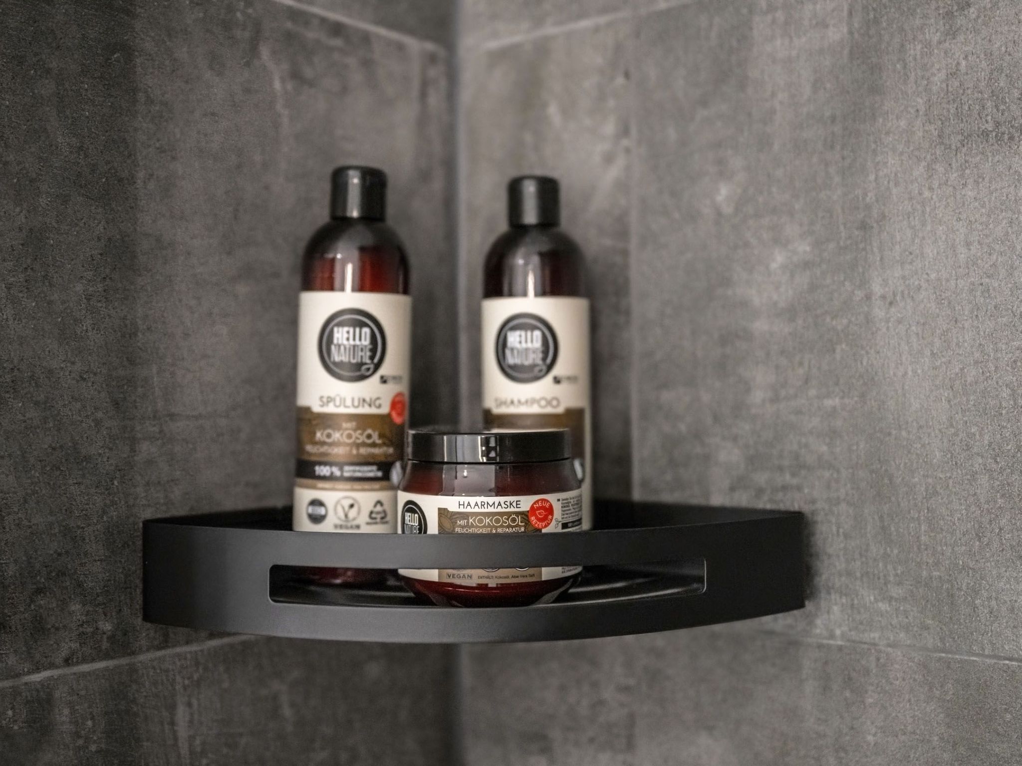 Un estante de baño con dos botellas de productos capilares 'Hello Nature' y un tarro de mascarilla para el cabello.