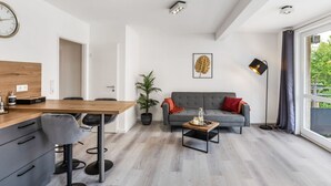 Een moderne woonkamer met een houten eettafel, een grijze bank en een groot raam met uitzicht op groen.