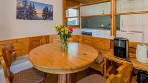 Ein gemütlicher Essbereich mit Holztisch und -stühlen, einer Vase mit Blumen und einer Küche im Hintergrund.