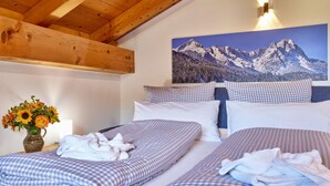Quarto de hotel com duas camas, roupa de cama xadrez, pintura de montanhas, um vaso com girassóis e teto de madeira.