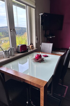 Un'area pranzo moderna con tavolo in vetro, un centrotavola con una mela rossa e vista all'esterno attraverso ampie finestre.