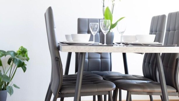 A dining area with a table set for four, surrounded by dark leather chairs. There is a potted plant on the left and a vase with flowers on the table. - mit privat Hottub und Klima. by Interhome (Neubörger)