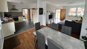 A modern apartment with a kitchen, dining area, and living room. It features a large dining table, grey sofas, and a TV in the living area. - mit privat Hottub und Klima. by Interhome (Neubörger)