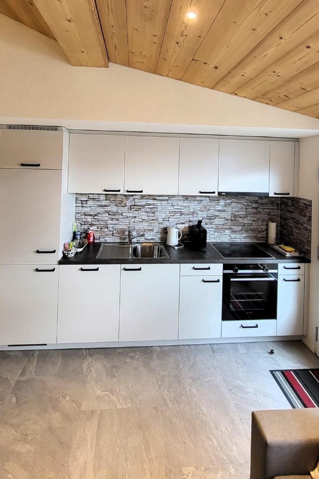 Une cuisine moderne avec des armoires blanches, un pare-feu en pierre et une cuisinière noire.