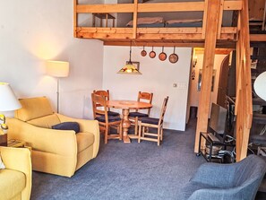 A loft-style room with a wooden bunk bed, a dining table with chairs, a sofa, and a lamp.