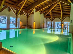 Una piscina interior con vigas de madera y ventanas amplias.
