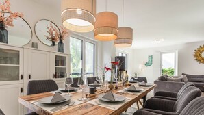 Uma sala de jantar moderna com uma mesa de madeira posta para seis pessoas, cercada por cadeiras estofadas cinzas.