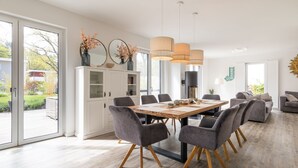 Uma área de refeições moderna com uma mesa de madeira, cadeiras estofadas cinzentas e luminárias pendentes.