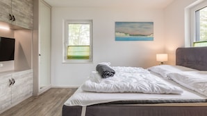 Quarto moderno com cama, janela com vista, quadro na parede e televisão à esquerda.