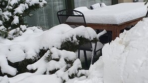 A snow-covered outdoor area with a wooden table and chairs, a snow-covered tree, and a building with large windows in the background. - Haus Goodewind by Interhome (Ahlbeck)