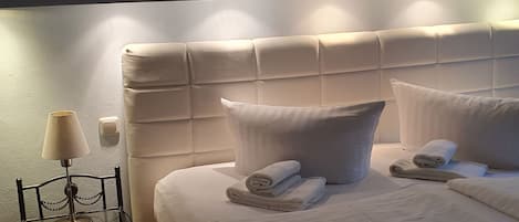Un lit bien fait, avec des oreillers et des serviettes pliées, une lampe de chevet et une petite table avec une lampe.