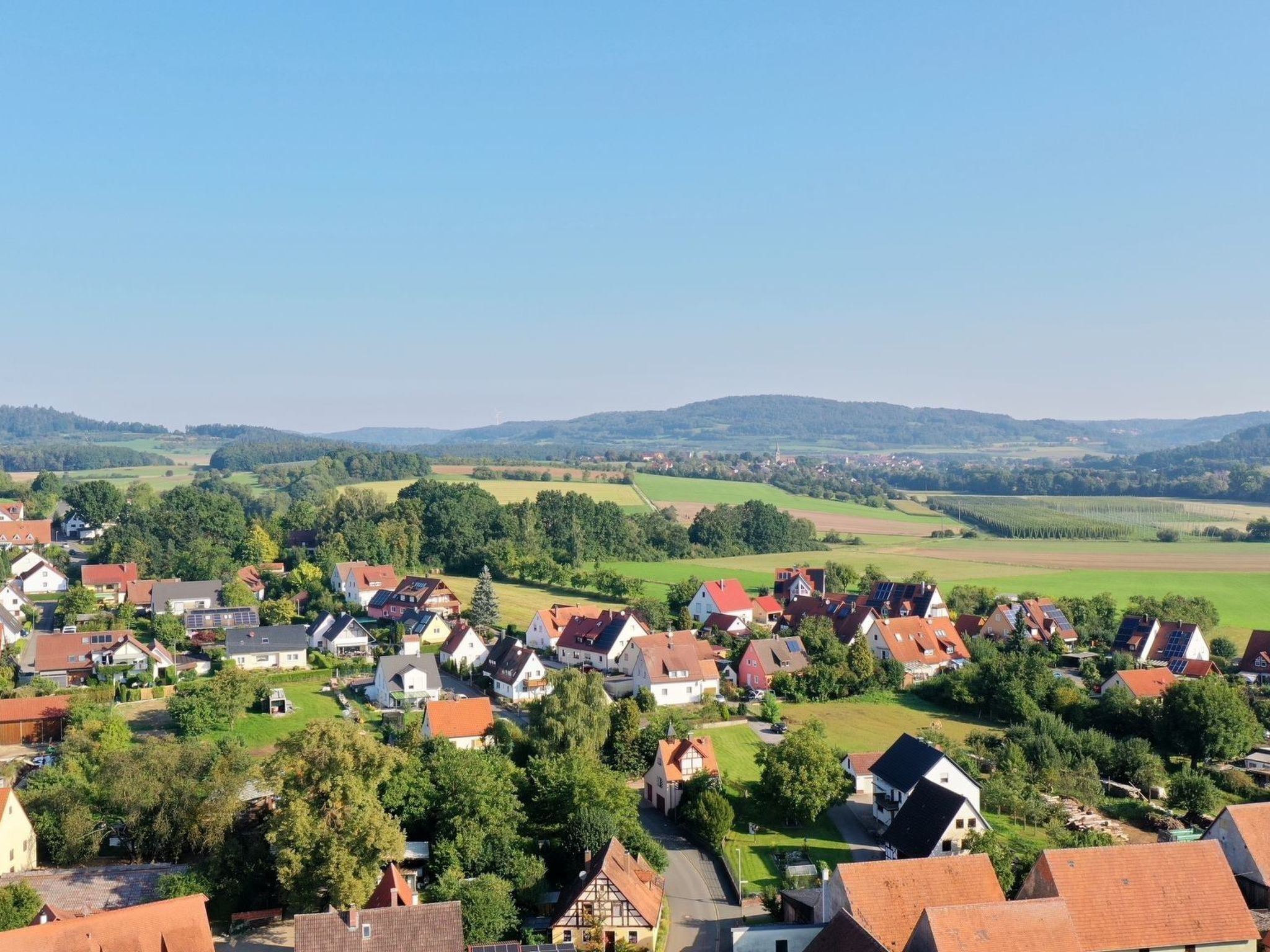 A rural village with traditional houses, a clear sky, and green fields in the background.