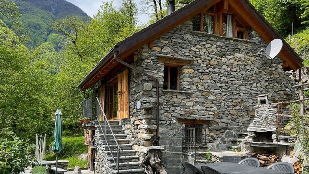 A stone cabin with a wooden exterior, a chimney, and a satellite dish.