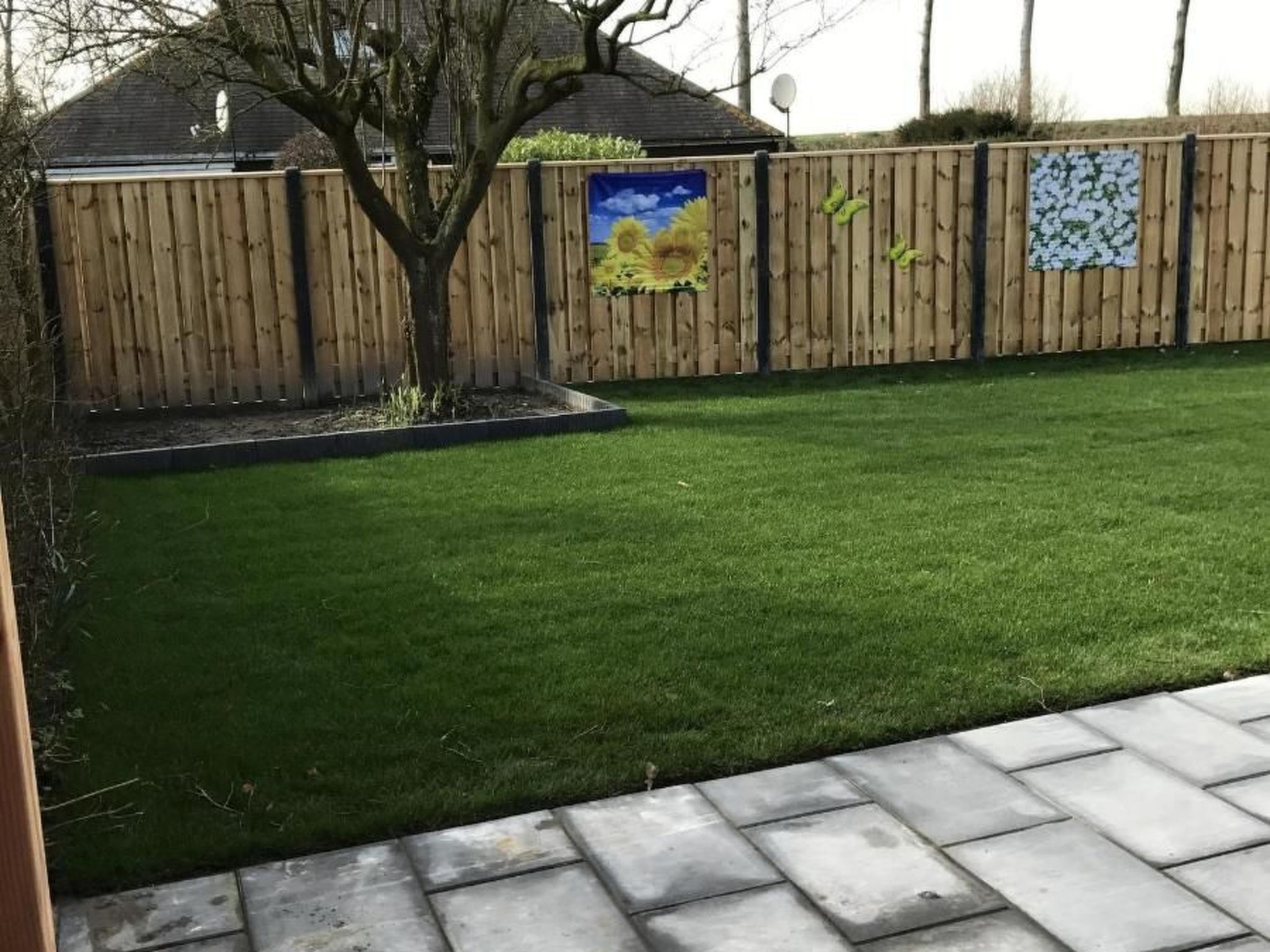 Un jardin bien entretenu, avec une clôture en bois, un petit arbre et une pelouse verdoyante.