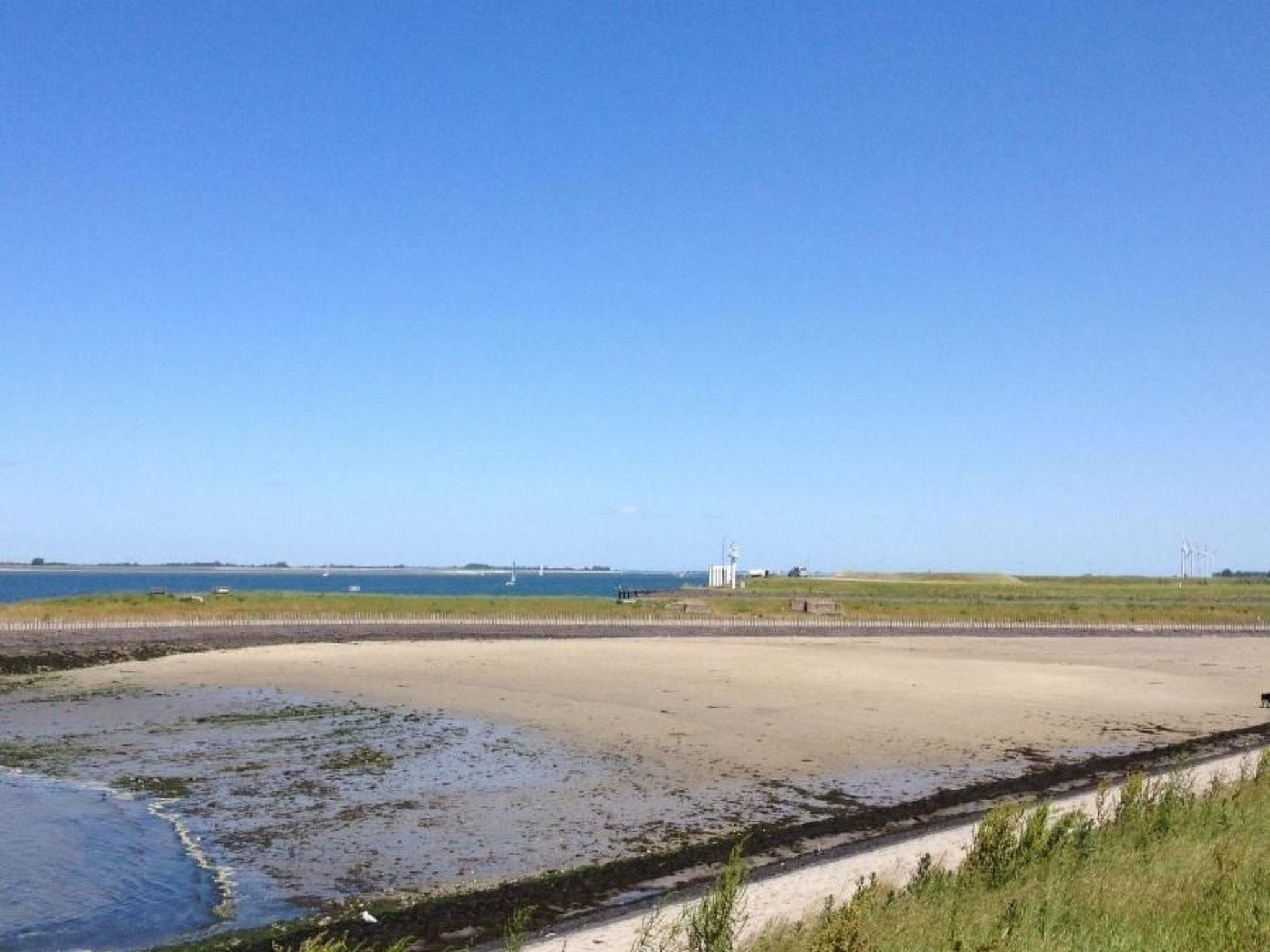 A coastal landscape with a sandy beach, a lighthouse, and wind turbines in the distance.