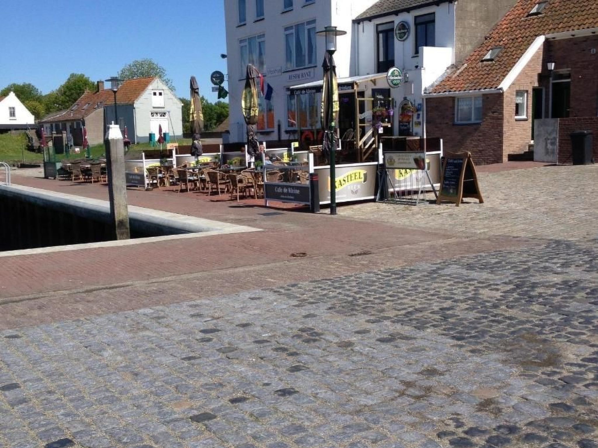 Una calle empedrada con mesas al aire libre y un café llamado 'Café de Marine'.