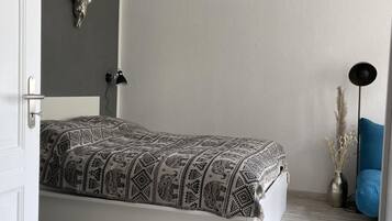 Ein schlichter Schlafzimmer mit Bett, einer Pendelleuchte, einer Wanddekoration in Form eines Schädels und einem kleinen Nachttisch mit einer Vase.