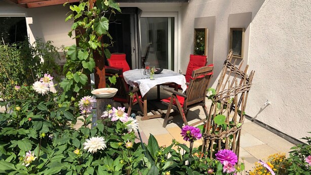 An outdoor patio with a table and chairs, surrounded by various plants and flowers.