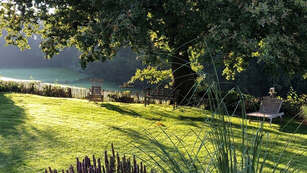 A well-maintained garden with a lawn, a wooden bench, and a chair near a fence.
