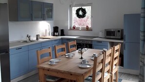 A modern kitchen with blue cabinets, a wooden dining table, and a window with a wreath. - Haus Bernstein by Interhome (Damshagen)