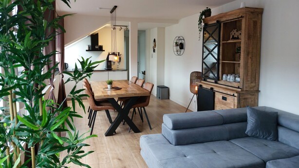 Uma sala de estar moderna com uma mesa de jantar de madeira, um sofá cinza e um armário de madeira com prateleiras.