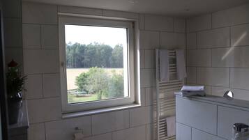 Ein Badezimmer mit großem Fenster, weißen Fliesen und einem Handtuchhalter sowie einem Waschbecken.