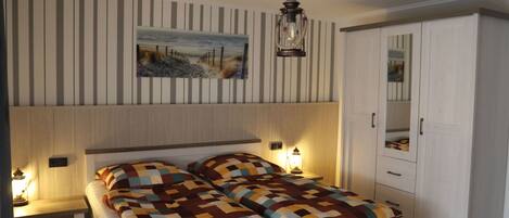 Un dormitorio con cama, mesitas de noche, armario, lámpara colgante y un cuadro en la pared.