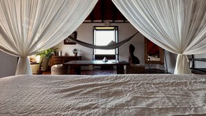 Un dormitorio con una cama grande, una hamaca y vistas al exterior a través de una ventana.