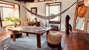 Una habitación acogedora con techo de madera, una hamaca, una mesa de madera, un banco, un espejo y una ventana con vistas.
