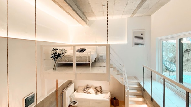 A modern interior with a staircase leading to a loft bedroom, a sofa bed, and a view of the outdoors.