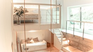 A modern loft-style apartment with a loft bed, a sofa, a dining area, and a staircase.
