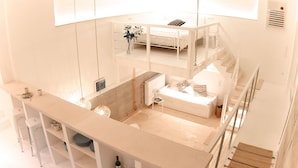A modern, open-plan living space with a kitchen area, a dining table, and a sofa. There is a staircase leading to an upper level.