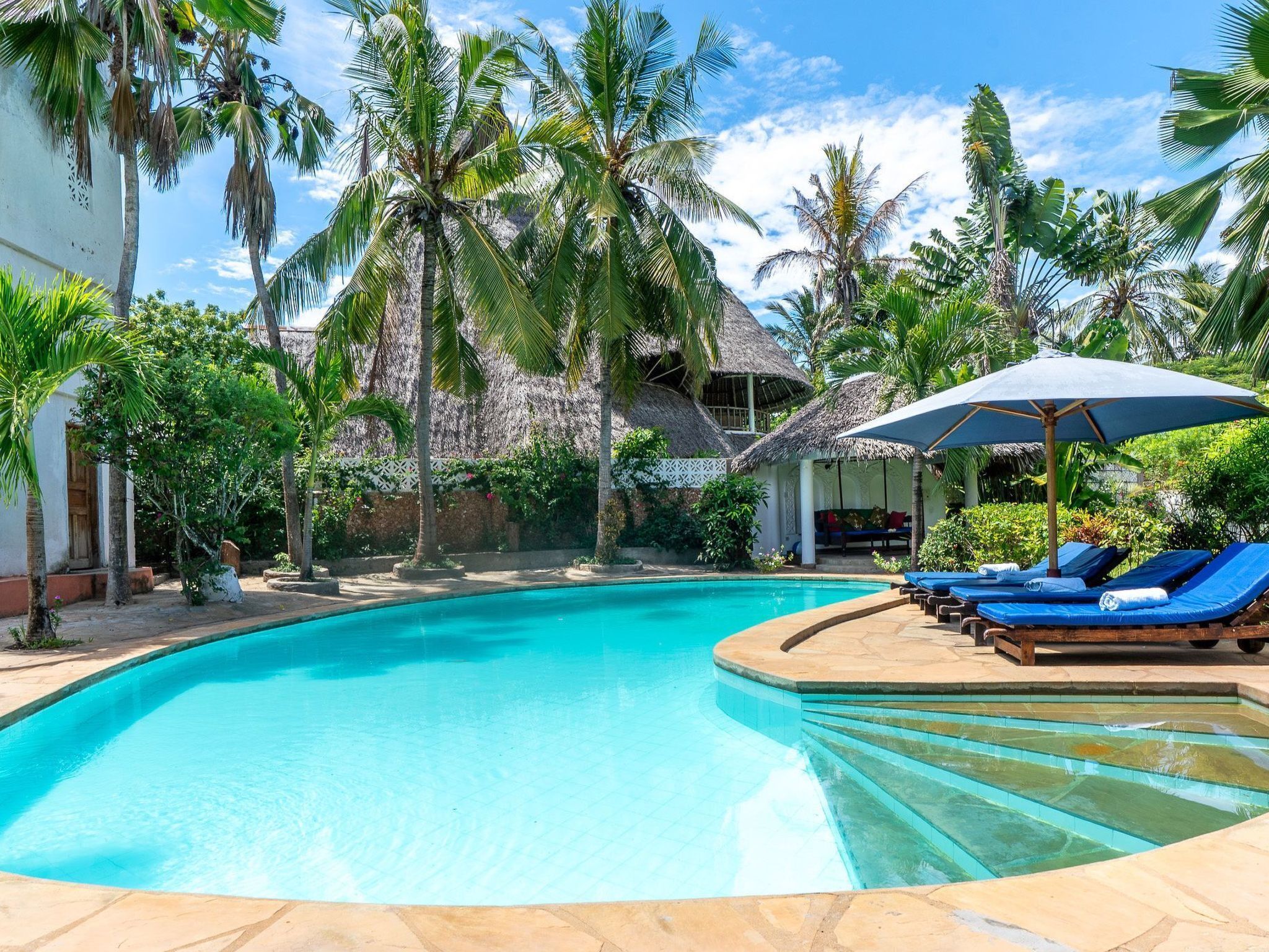 A clear blue pool surrounded by palm trees and a thatched-roof structure.
