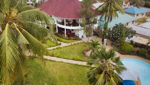 A two-story house with a red roof, surrounded by lush greenery and palm trees.