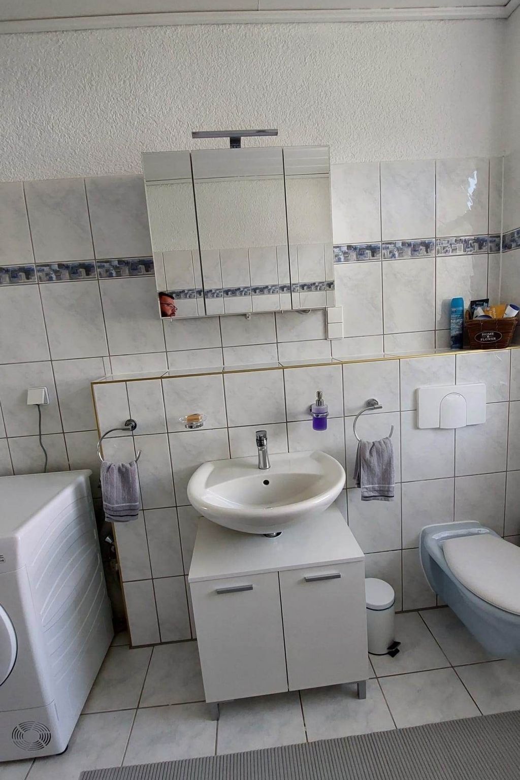 Un bagno con lavandino bianco, specchio e servizi igienici. È presente un porta asciugamani e un piccolo ripiano con articoli da toilette.