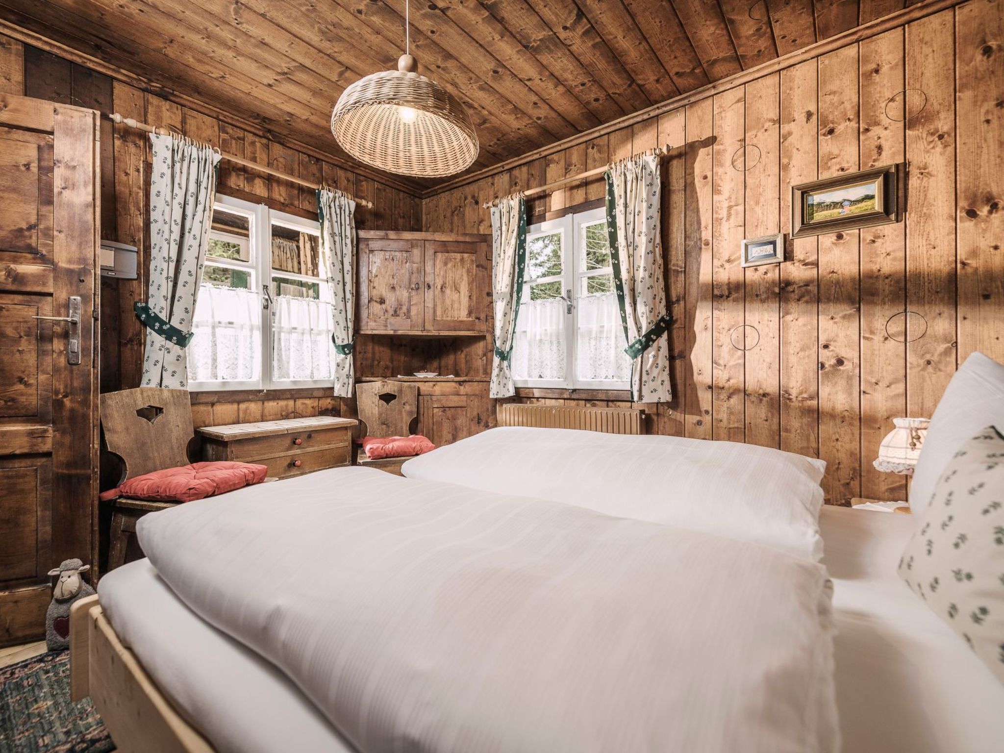Ein Zimmer in einer Holzhütte mit einem Bett, zwei Stühlen, einem kleinen Tisch und einer Hängelampe.