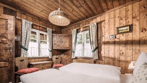 A wooden cabin room with a bed, two chairs, a small table, and a hanging light fixture. - Berg Hütte Hochpillberg by Interhome (Pill)
