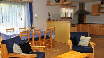 Ein gemütliches Wohnzimmer mit Essbereich, Holzmöbeln und einer Küche im Hintergrund.