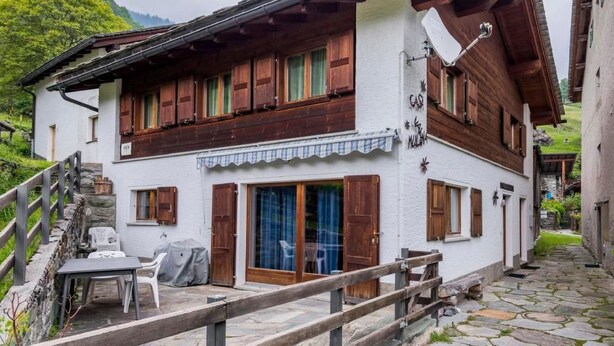 Eine zweistöckige Chalet mit Holzläden, einer Steintreppe und einem kleinen Sitzbereich im Freien.