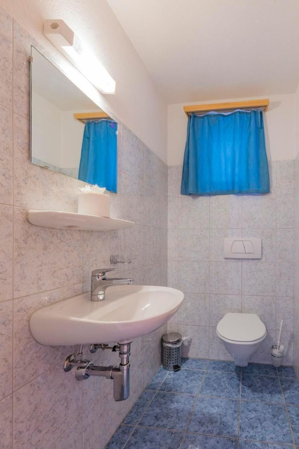 Ein Badezimmer mit weißem Waschbecken, einem Spiegel, einem blauen Duschvorhang und einer Toilette.