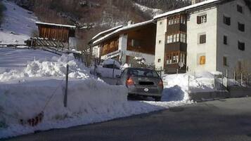 Un bâtiment doté d’un toit en pente, une voiture garée devant et un paysage enneigé.