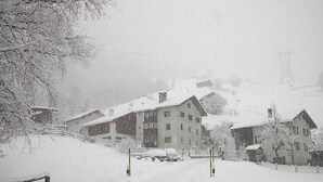 Eine verschneite Straße mit Gebäuden, darunter ein mehrstöckiges Hotel und eine Seilbahn im Hintergrund.